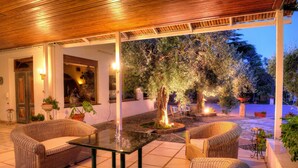 An outdoor patio with wicker furniture, a glass table, and a central tree illuminated by lights. - Scilla e Cariddi Bed&Breakfast (Messina)