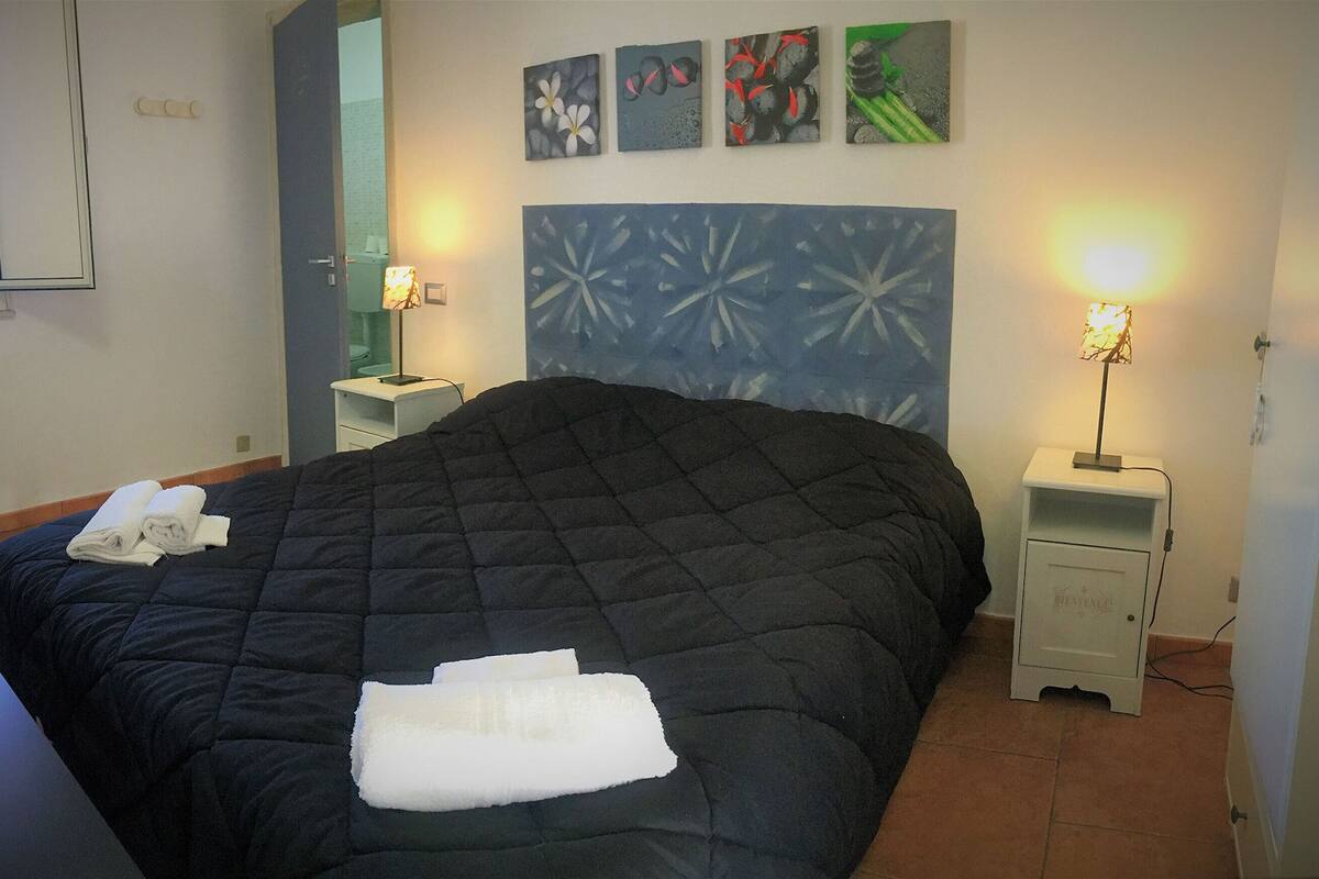 Un dormitorio con una cama grande, dos mesitas de noche, una lámpara de pared y obras de arte.