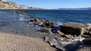 A coastal scene with a rocky shoreline, clear blue water, and a distant town on a hill. - Scilla e Cariddi Bed&Breakfast (Messina)
