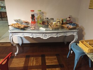 Een eettafel met verschillende soorten eten en verpakkingen, een blauwe stoel en een rieten mand.