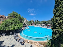 A large outdoor swimming pool with lounge chairs and umbrellas, surrounded by trees and buildings.