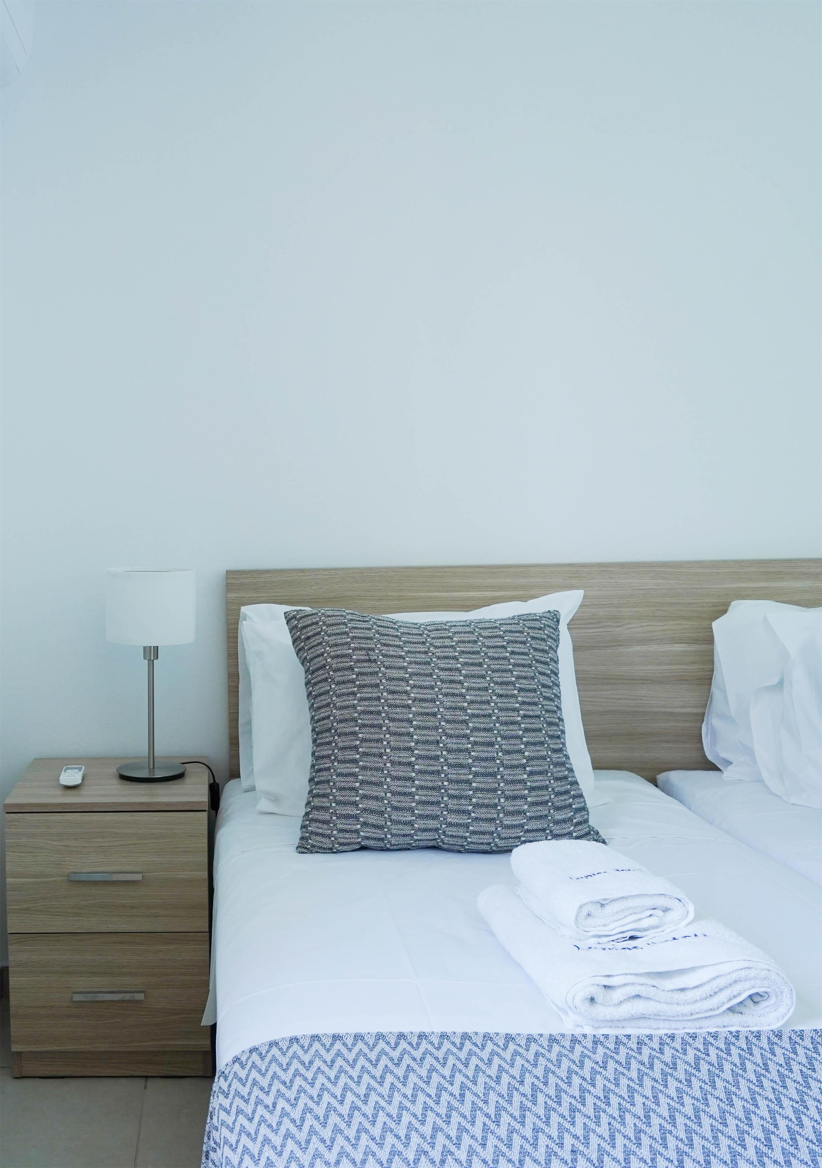 A neatly made bed with a patterned pillow, a white pillow, and a folded towel on a blue and white patterned bedspread.