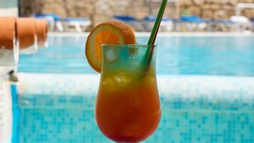 Un verre contenant une boisson, une tranche d’orange et une paille, posé au bord d’une piscine.
