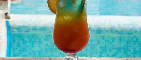 Un vaso de bebida con una rodaja de naranja y una pajita junto a una piscina.