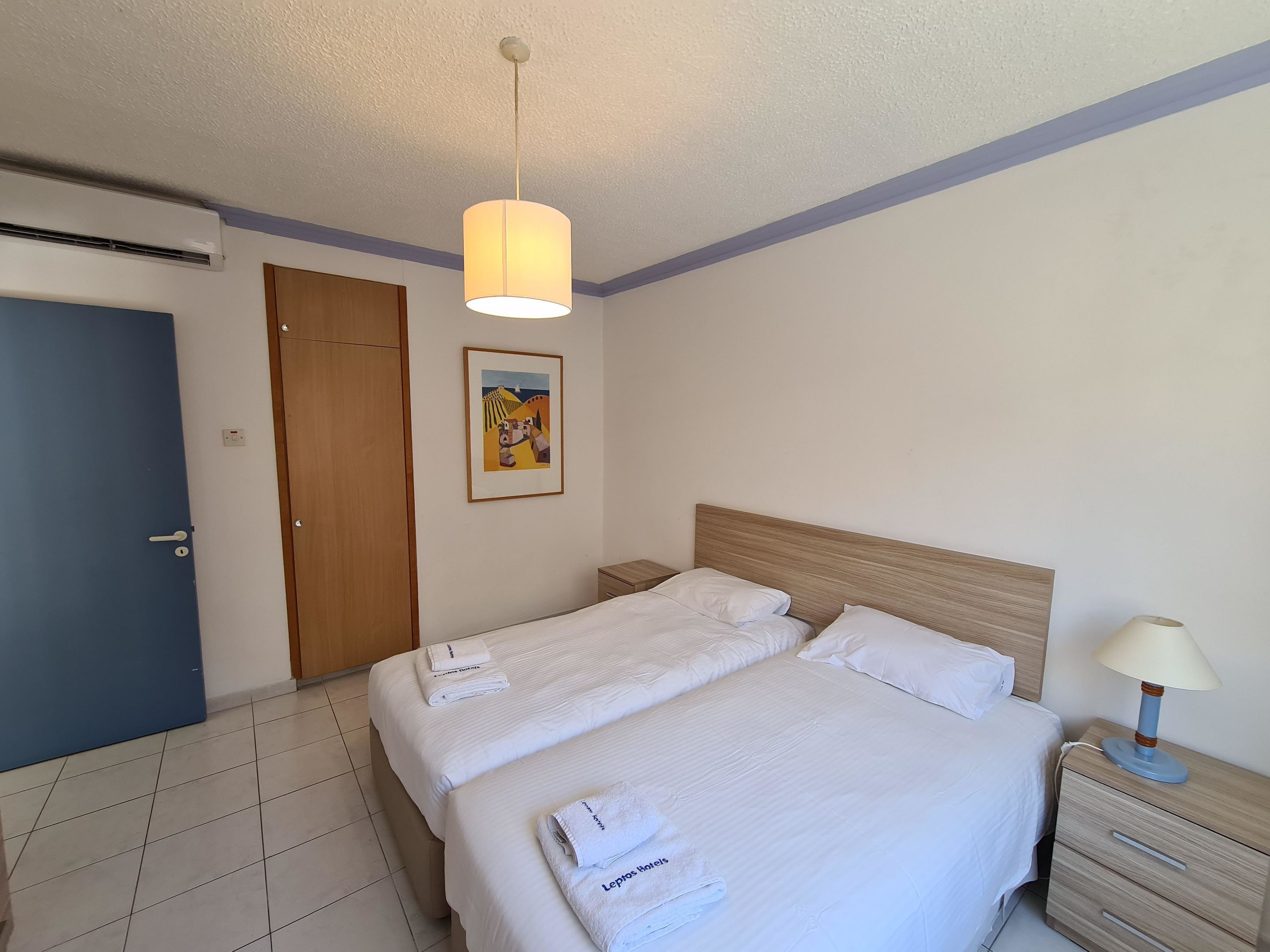 A hotel room with a bed, a nightstand, a lamp, a door, and a painting on the wall.