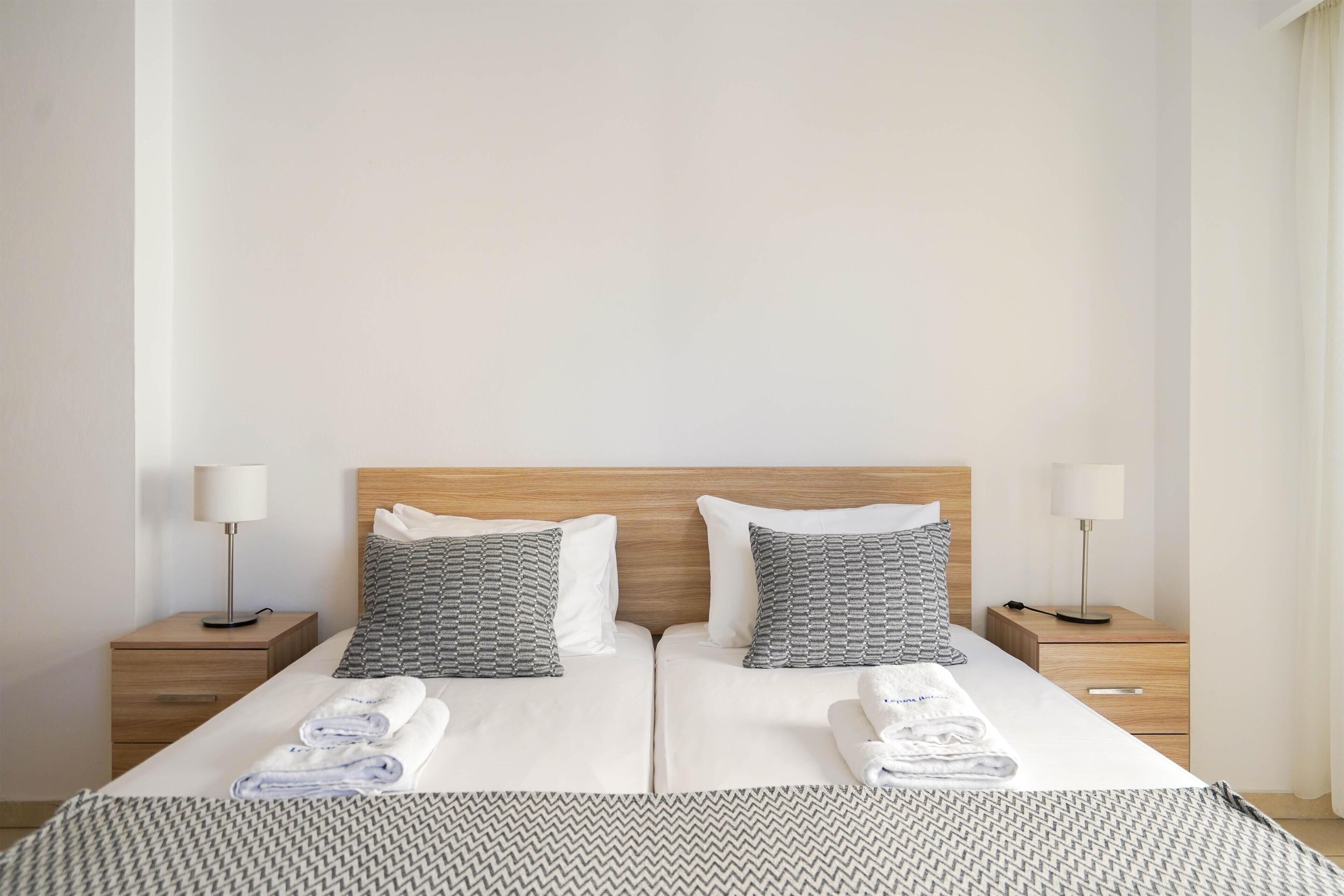 Ein Doppelbett mit zwei Kissen, ein Nachttisch mit Lampe und ein gefaltetes Handtuch auf dem Bett.