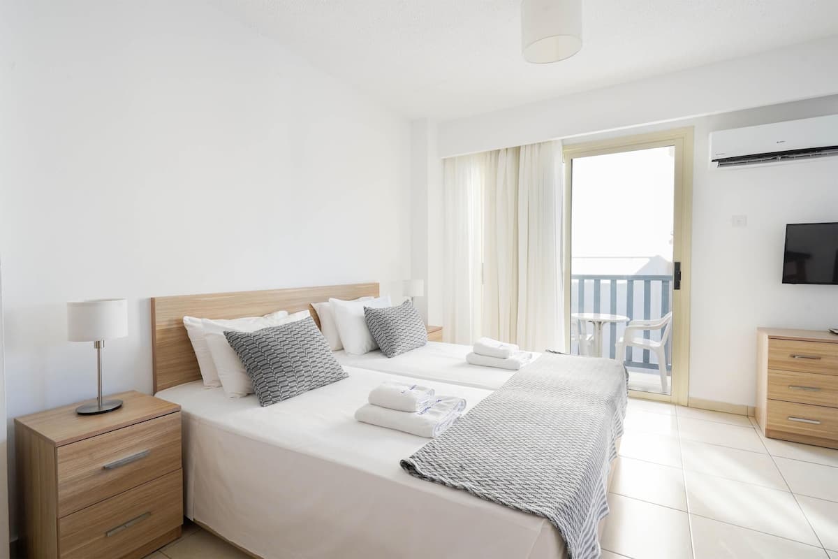 A hotel room with a large bed, two bedside tables, a TV, and a balcony with a view.