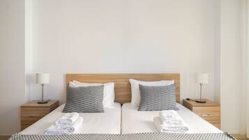 Quarto de hotel com cama de casal, duas mesas de cabeceira com luminárias e manta com padrão herringbone.