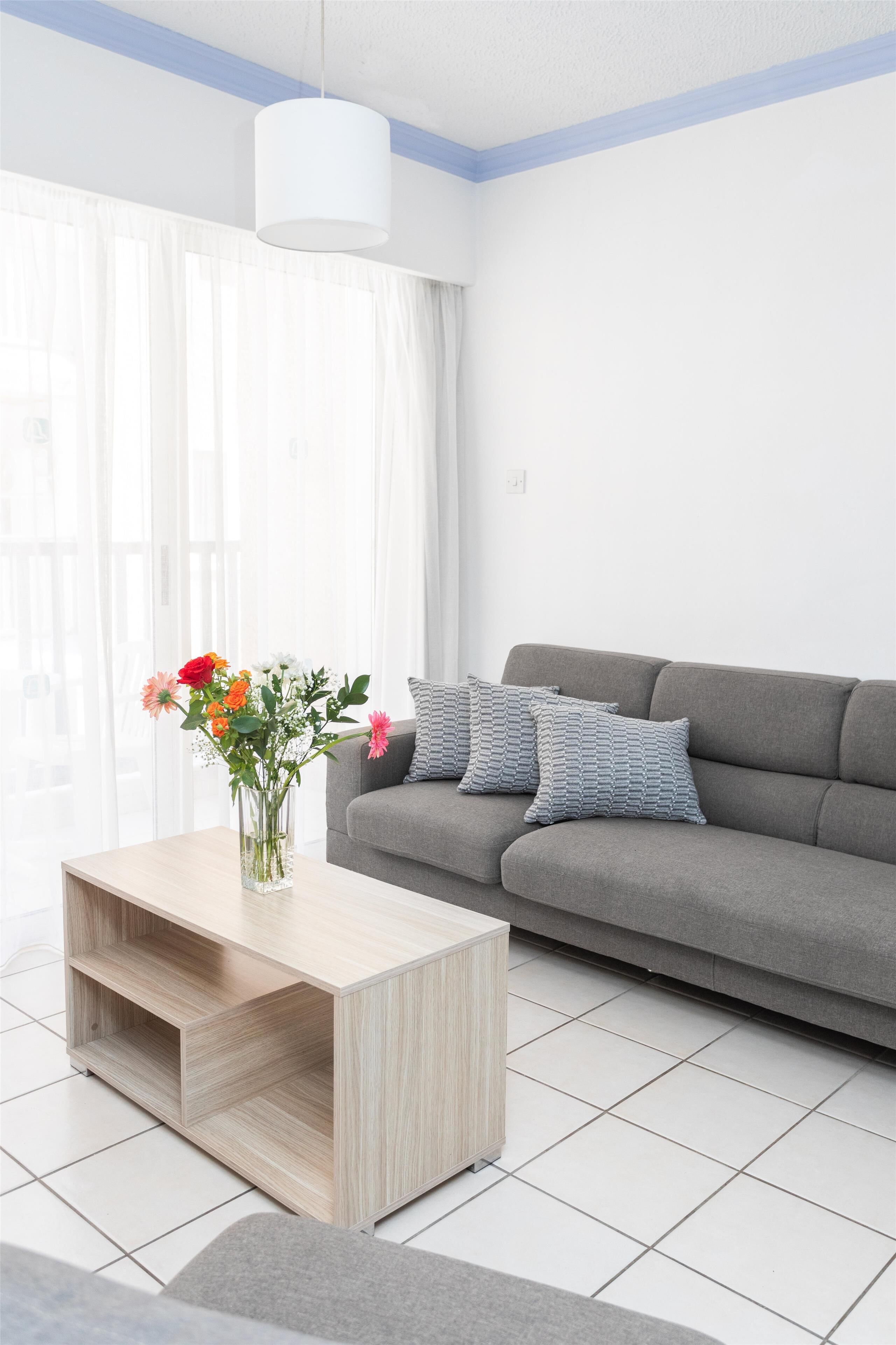 Un salon moderne avec un canapé gris, une table basse en bois et un vase de fleurs.