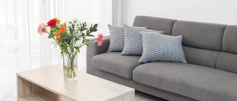 A modern living room with a grey sofa, a wooden coffee table, and a vase of flowers.