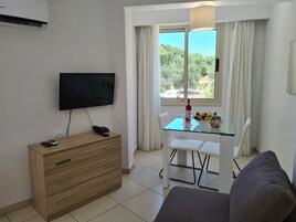 Una sala moderna con televisor de pantalla plana, un mueble de madera, una mesa de vidrio con sillas y un sofá.