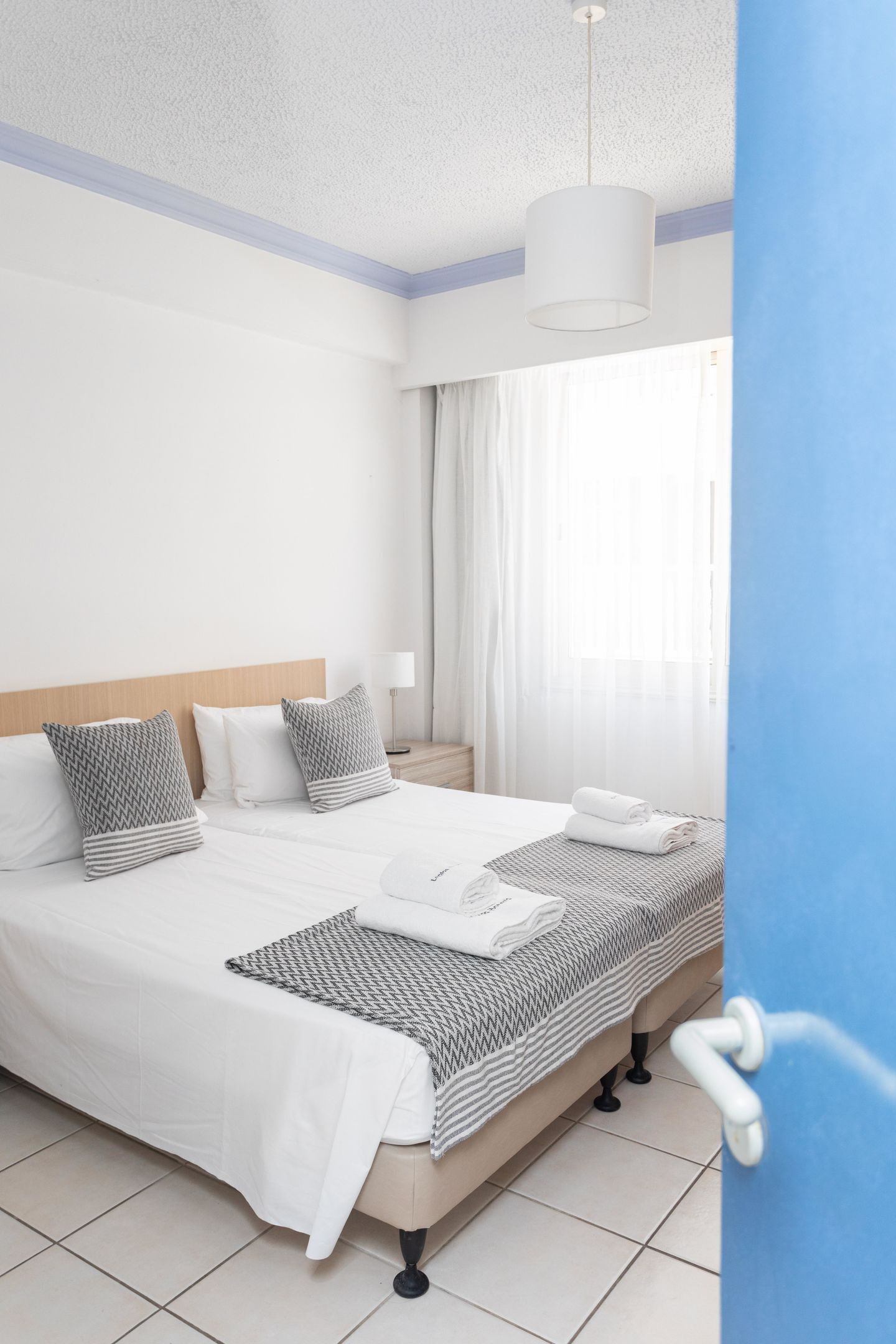 A hotel room with a bed, a nightstand, a lamp, and a window with curtains.
