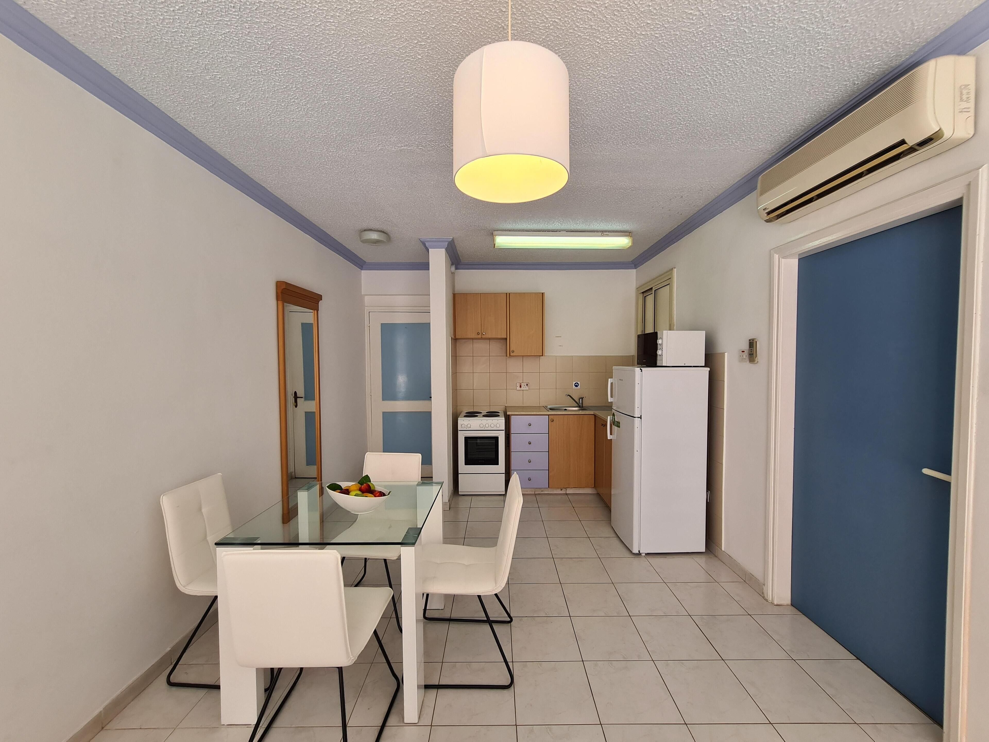 Una cocina compacta con comedor, electrodomésticos blancos y una puerta azul.