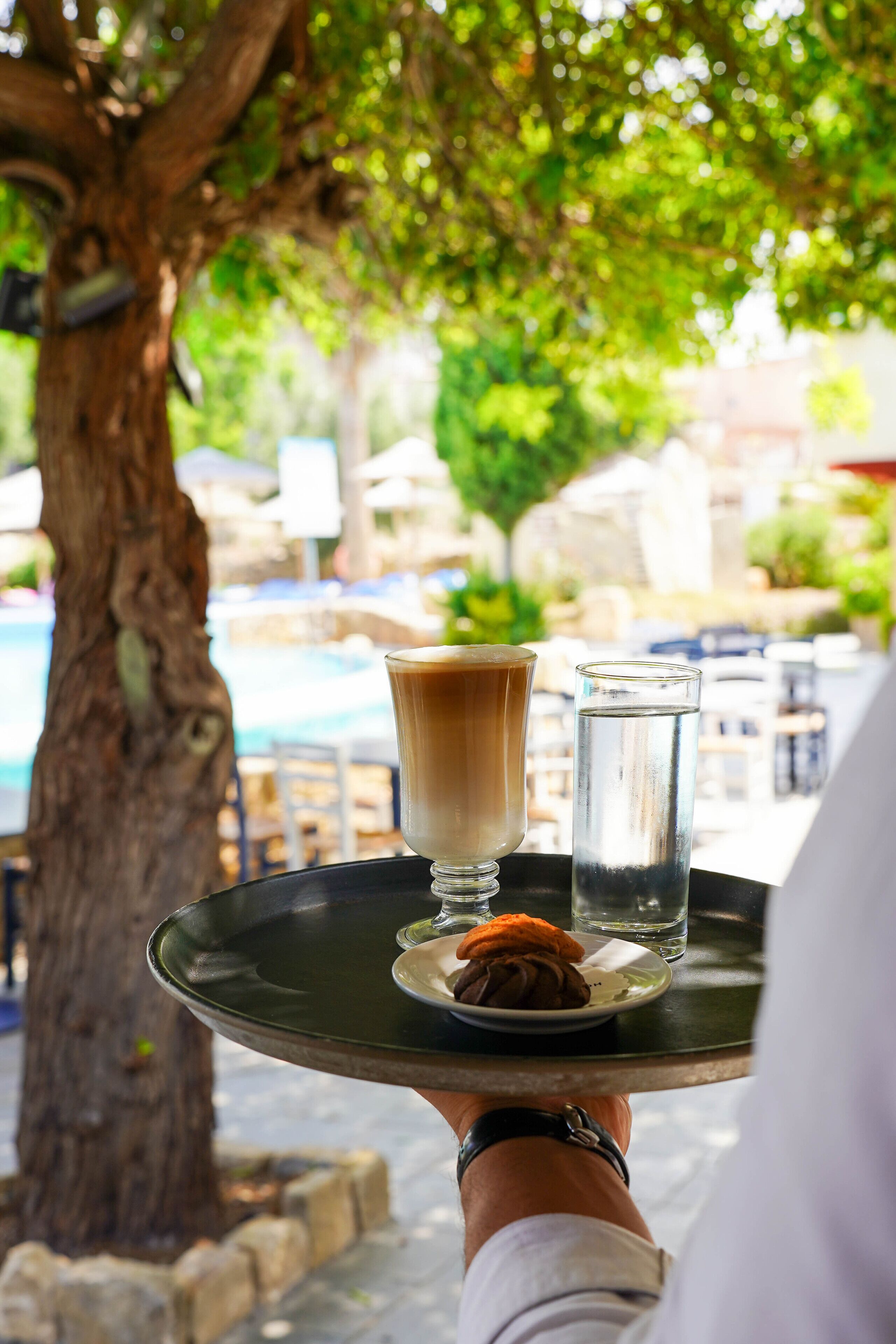 Un plateau avec une boisson chaude, un verre d’eau et un dessert, servis en plein air.