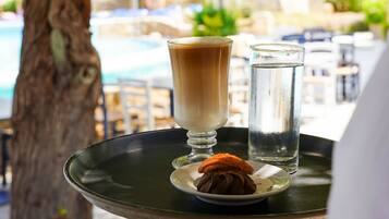 A tray with a hot beverage, a glass of water, and a dessert being served outdoors.