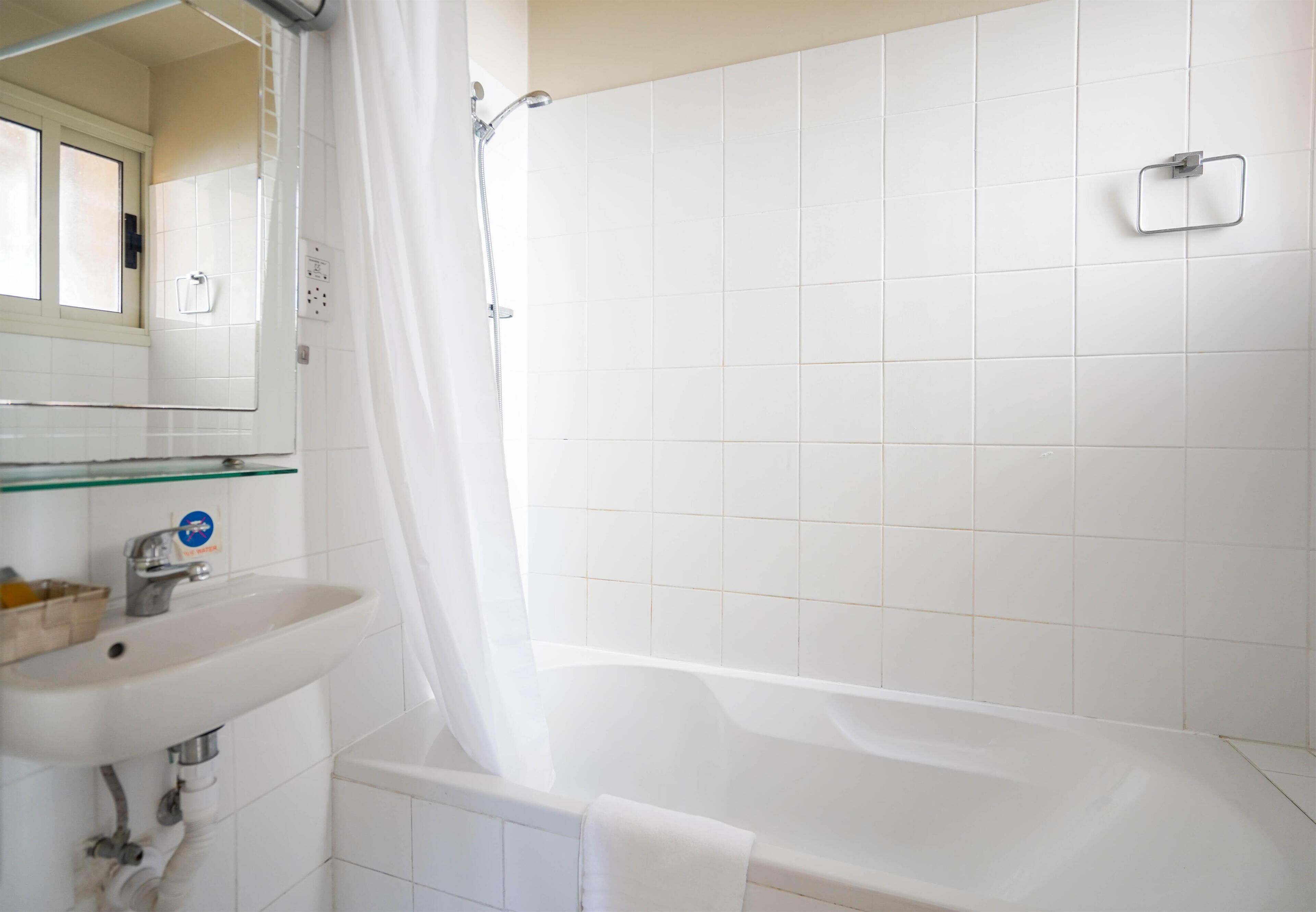 Ein Badezimmer mit einem weißen Waschbecken, einer Glasablage, einer Badewanne und einer Duschvorhang.