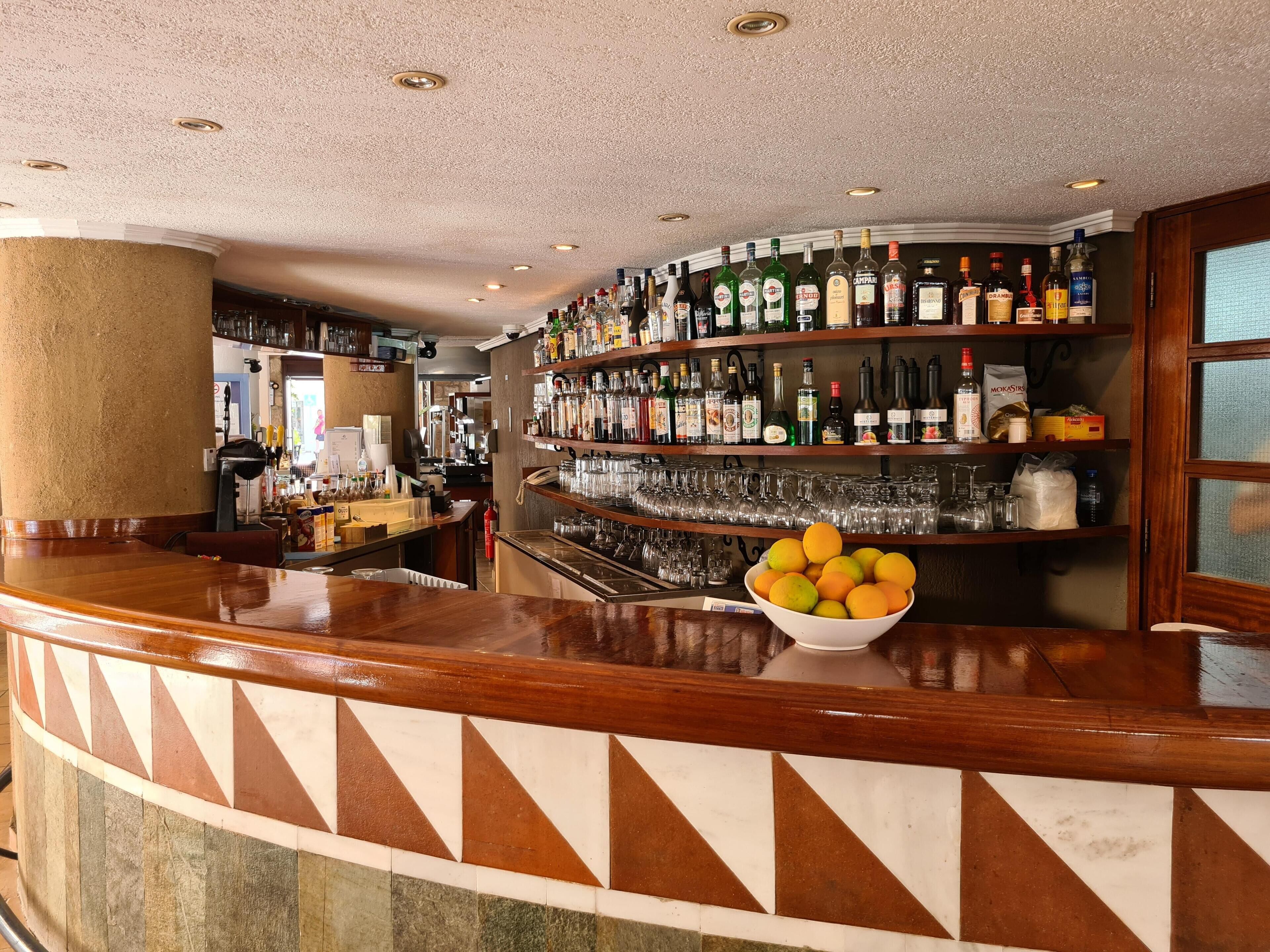 A bar area with a variety of liquor bottles, glasses, and a bowl of fruit on the counter.