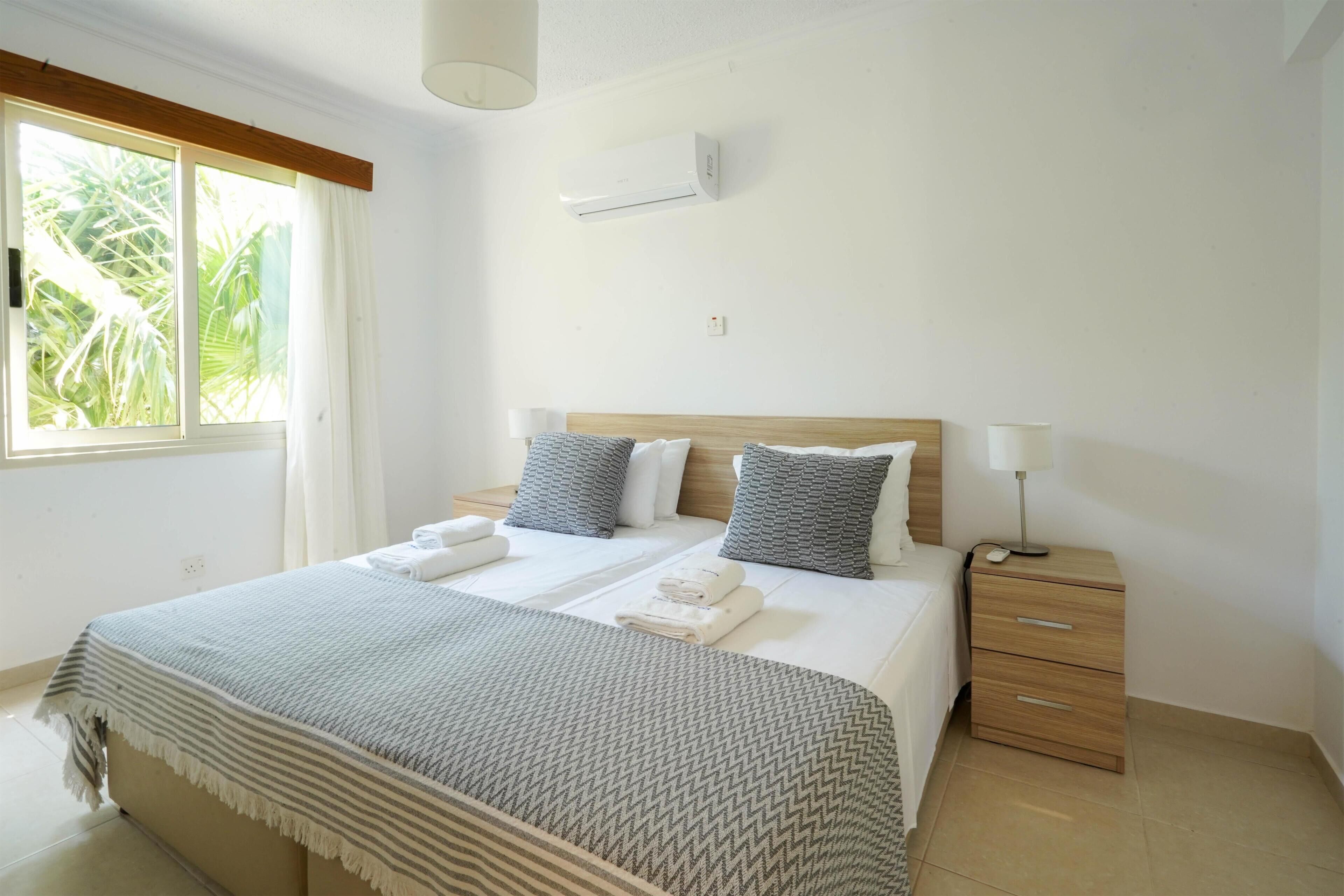 A neatly arranged bedroom with a large bed, bedside tables, and a window with curtains.