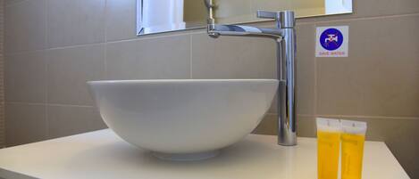 A bathroom with a large white basin, a faucet, and a 'Save Water' sign. There are two yellow tubes and two white caps on the counter.
