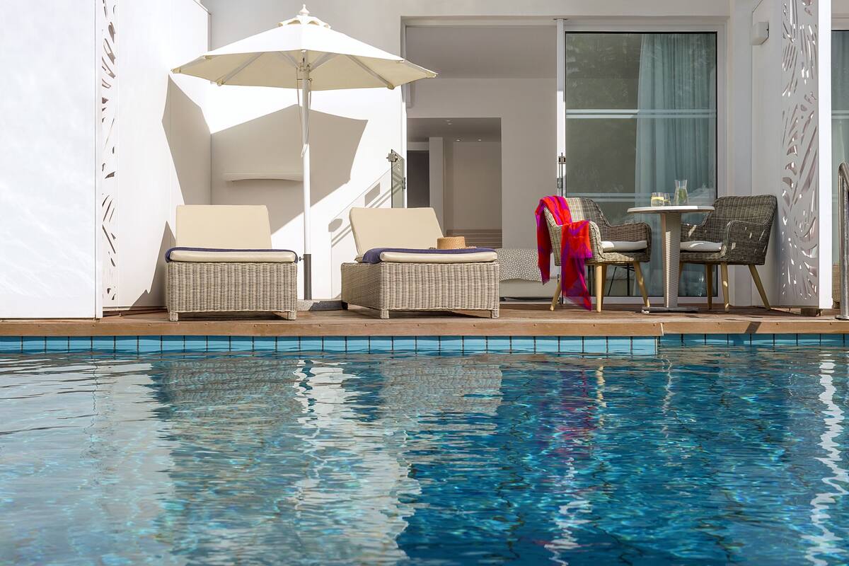 A poolside area with wicker lounge chairs, a table, and an umbrella.