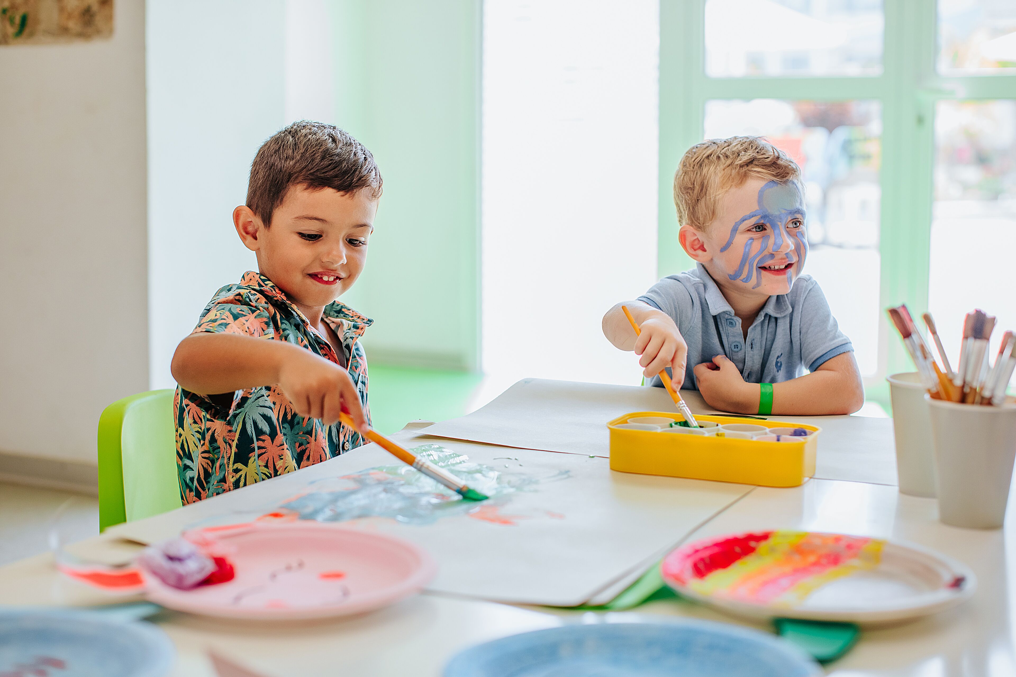 Two children painting at a table with art supplies.