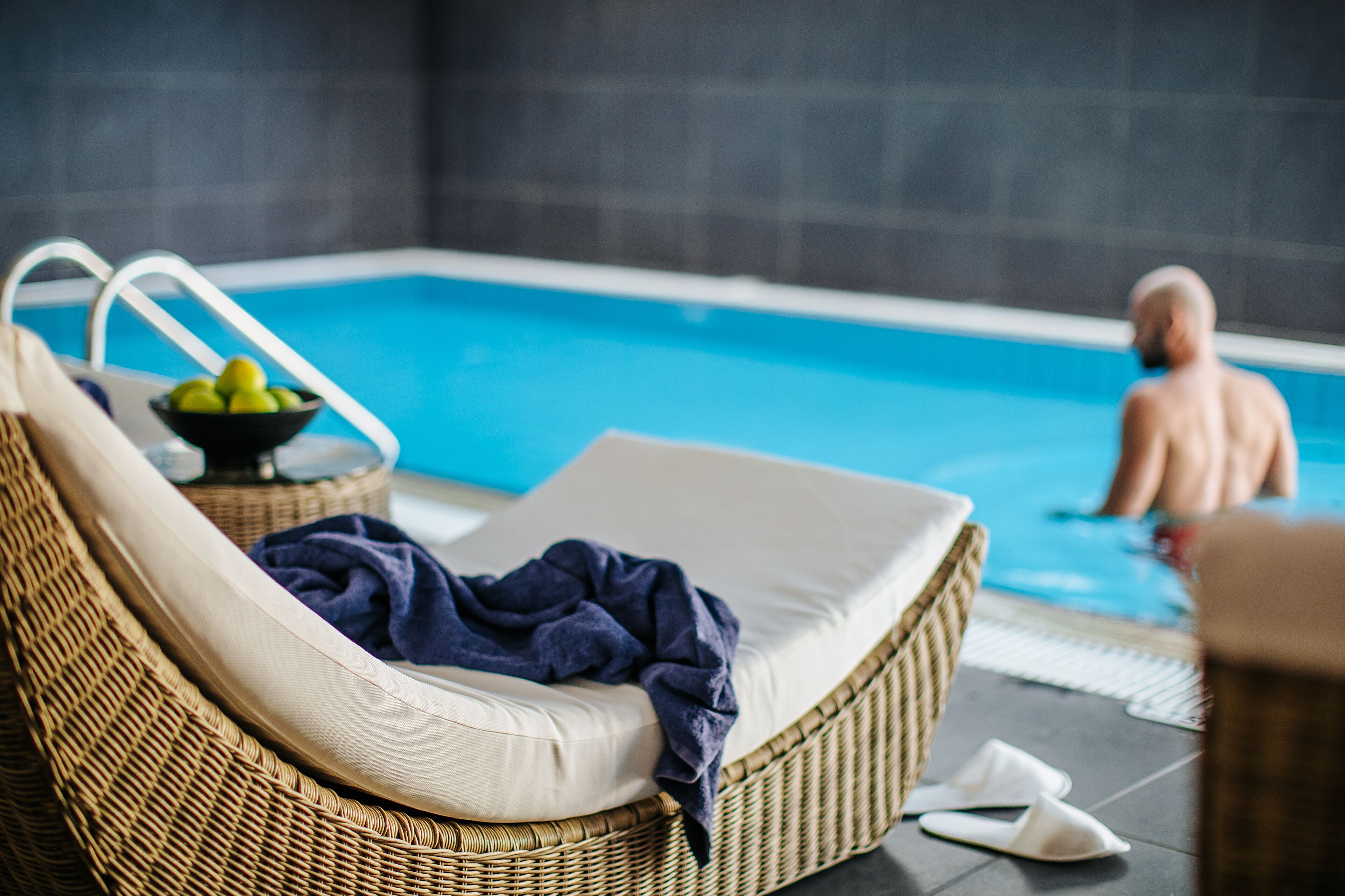 Un fauteuil de relaxation en osier, avec un coussin et un saladier rempli de fruits, placé près d’une piscine.