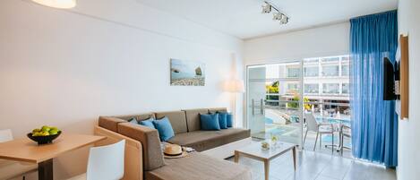 A modern living room with a sofa, dining table, and chairs. There is a balcony with a pool and a view of a building.