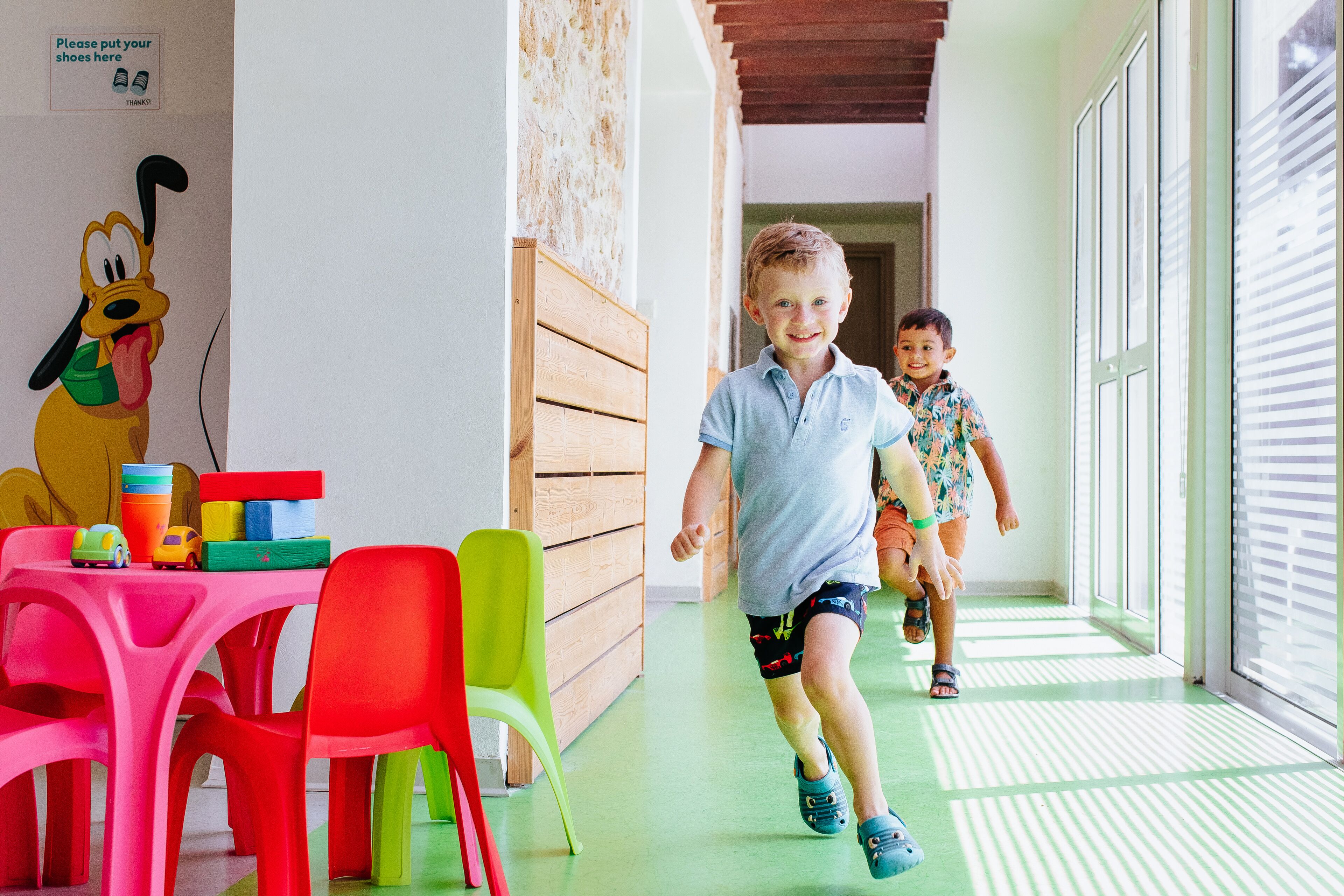 A hallway with a wooden bench, a table with colorful chairs, and a wall with a cartoon character.
