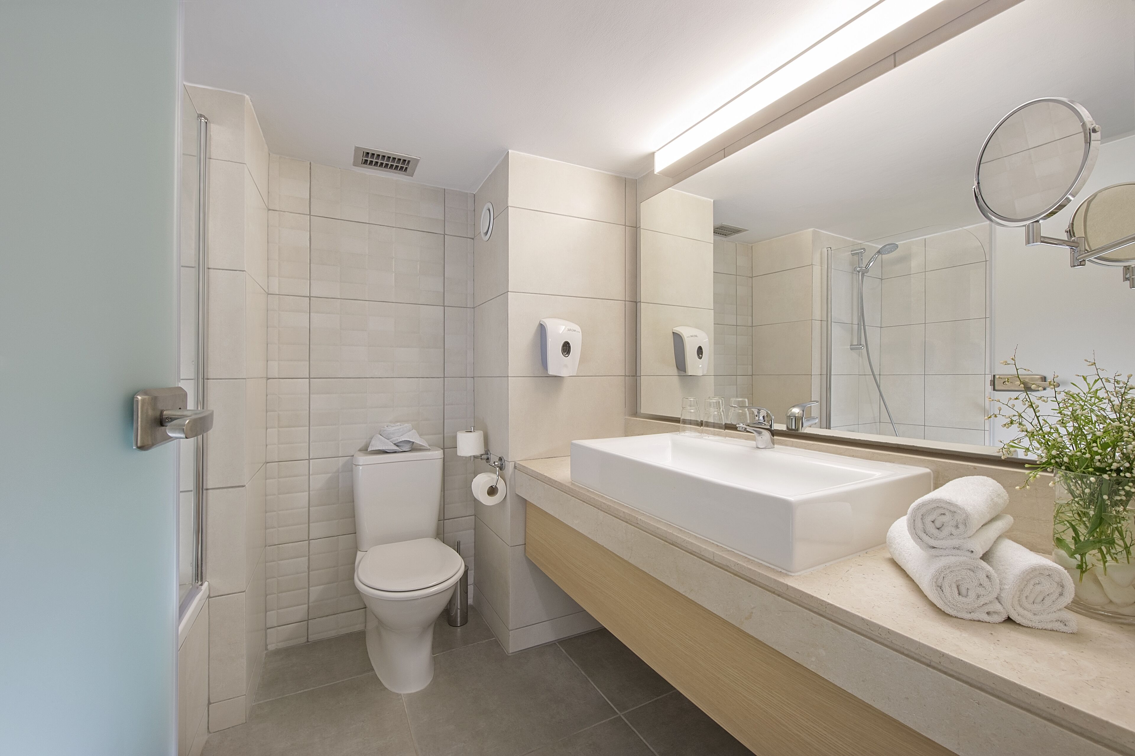 A modern bathroom with a toilet, bidet, and a large sink with a mirror above it.