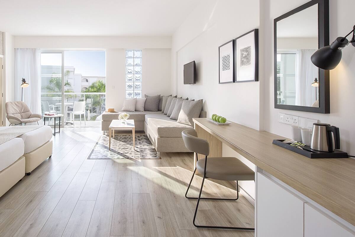 A modern hotel room with a bed, sofa, and a dining area.