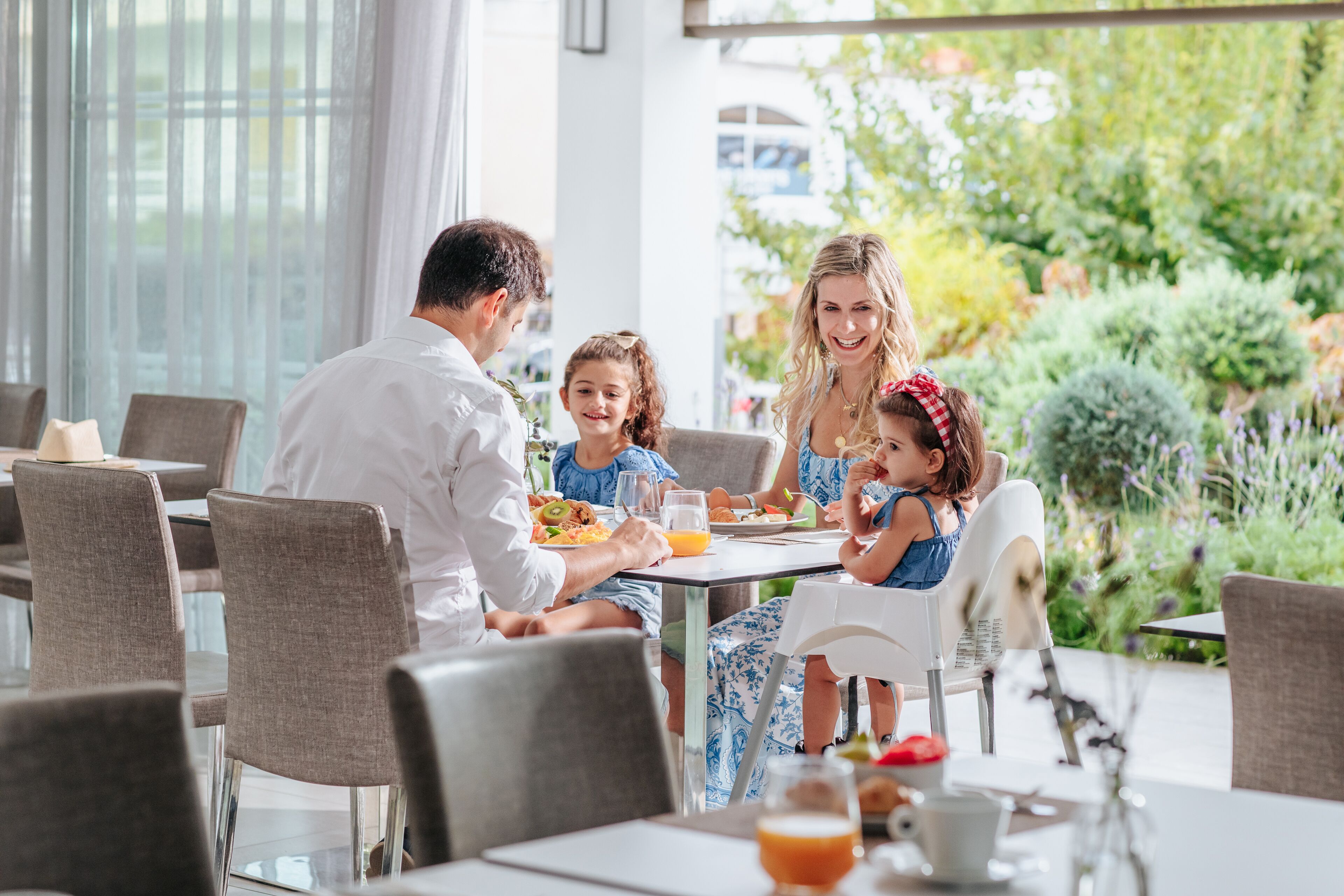A family dining at an outdoor restaurant with a view of greenery and a building in the background.
