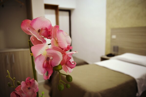 A hotel room with a bed, a nightstand, and a vase with pink flowers.