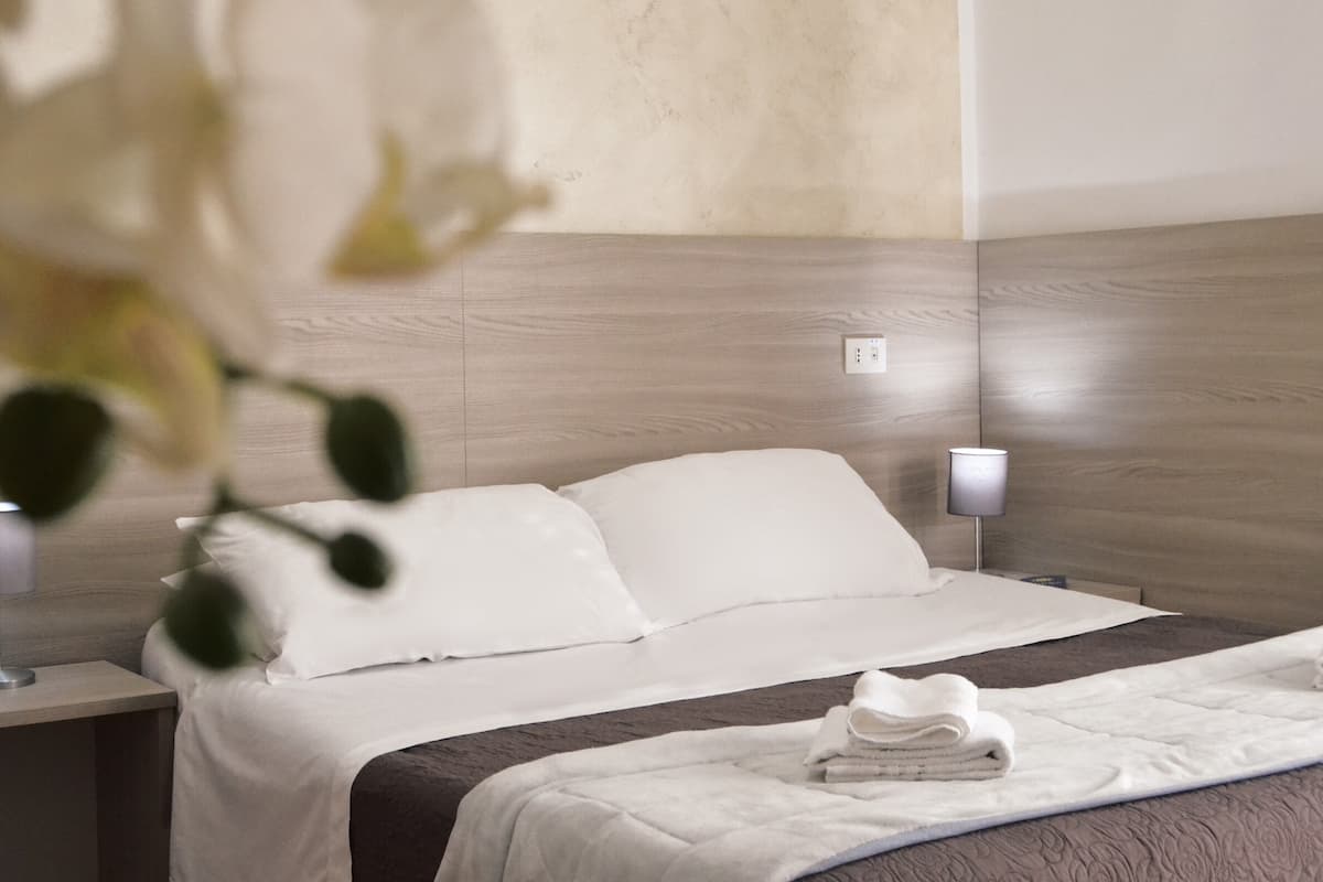 Une chambre d’hôtel avec une tête de lit en bois, un couvre-lit blanc et une serviette soigneusement pliée posée sur le lit.