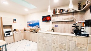 A hotel kitchen with a tiled floor, a coffee machine, and a TV on the wall. - Hotel Colombo (Naples)