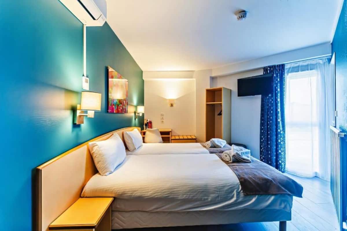 A hotel room with two beds, a desk, a chair, a TV, and a window with curtains.