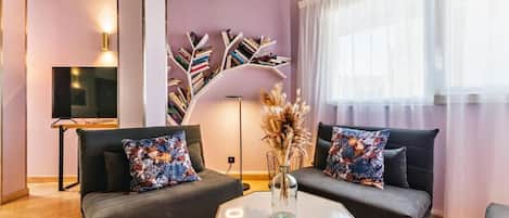 A modern living room with two dark sofas, a glass coffee table, and a unique bookshelf.