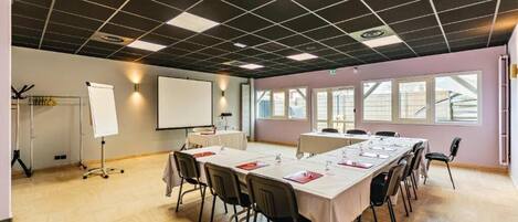 Un salón de conferencias con una larga mesa, sillas, una pizarra y una pantalla para proyector.