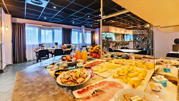 A buffet with various food items and beverages, a dining area with tables and chairs, and a kitchen in the background. - The Originals City, Hôtel Éclipse (Decines-Charpieu)