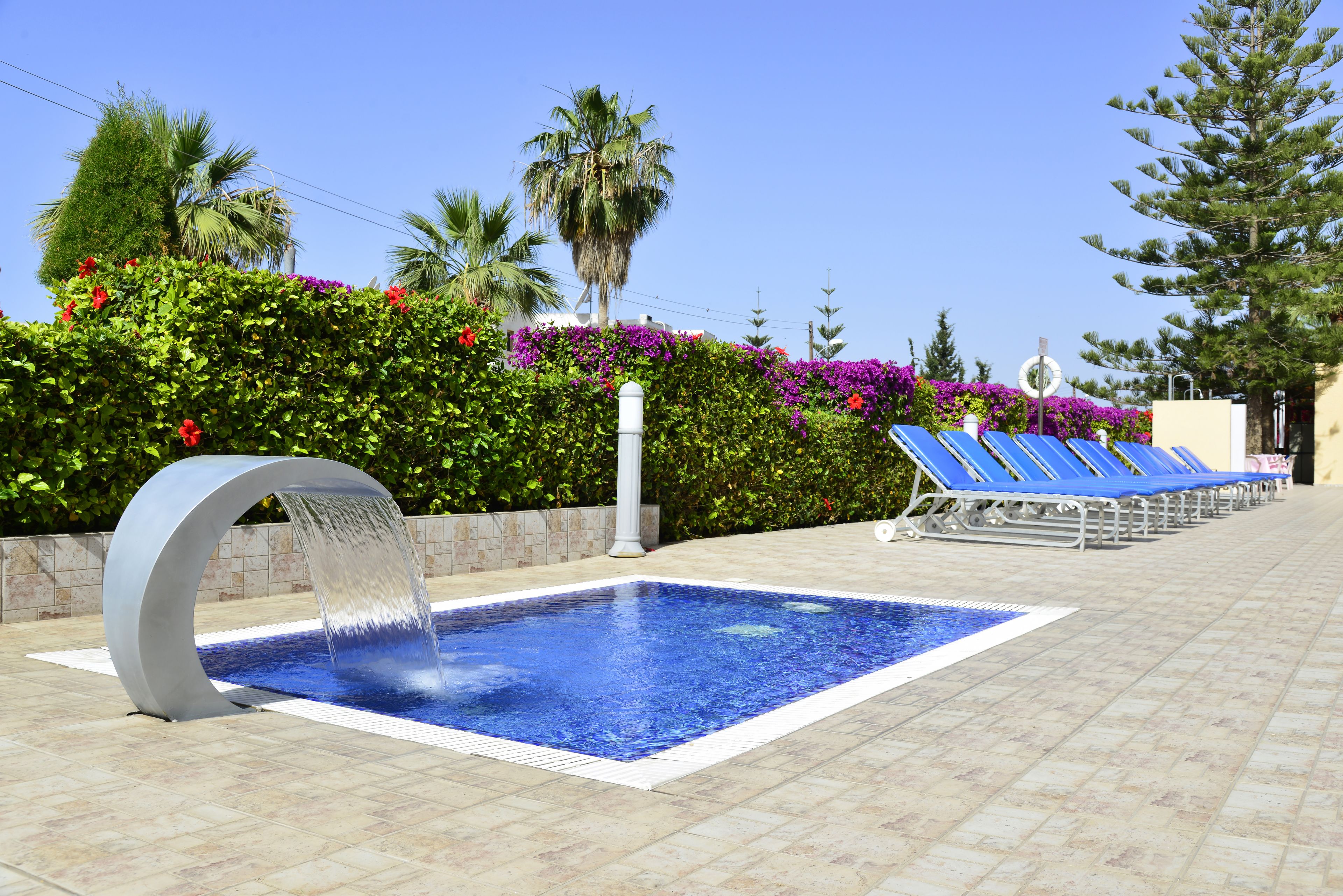 A swimming pool with a water feature, surrounded by a tiled deck and blue lounge chairs.