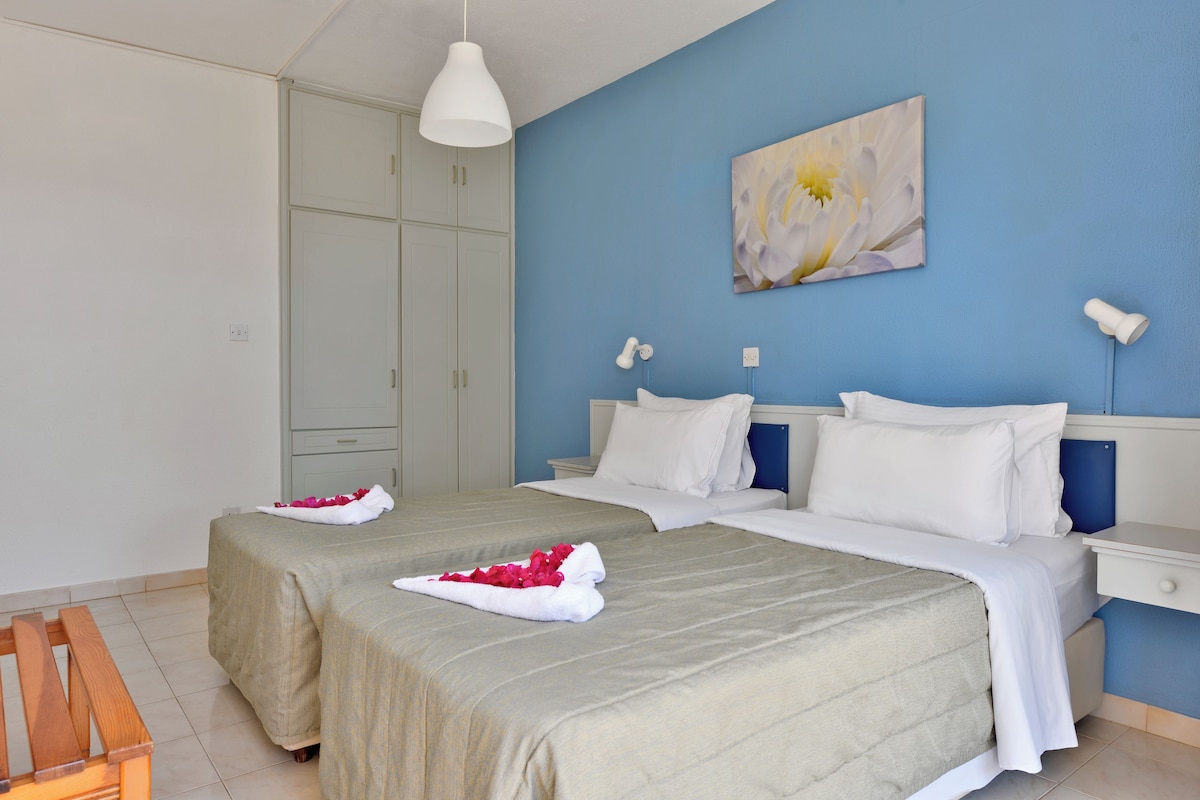 A hotel room with two beds, a wardrobe, and a painting on the wall.