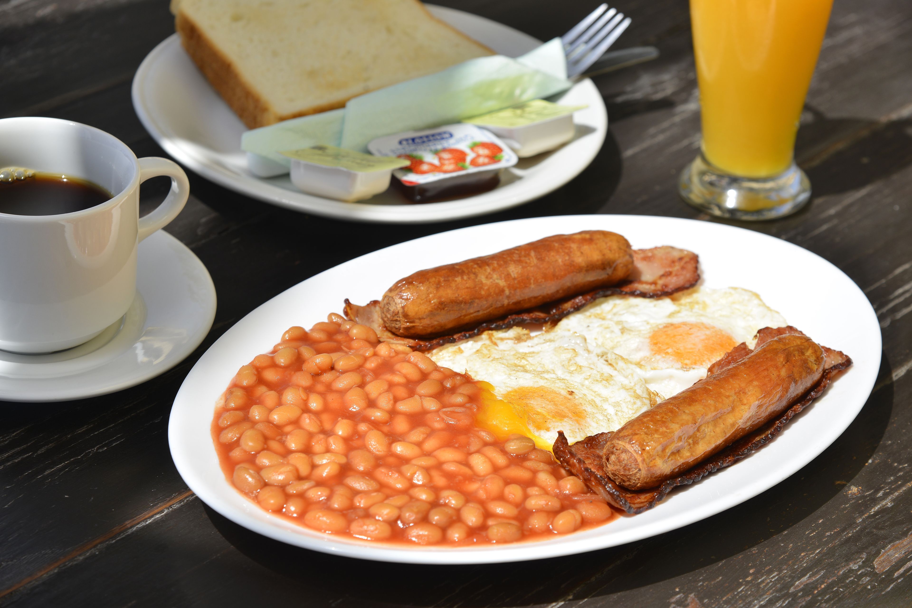Un plato de frijoles, salchichas y huevos sobre una mesa, con una taza de café y un vaso de jugo de naranja.