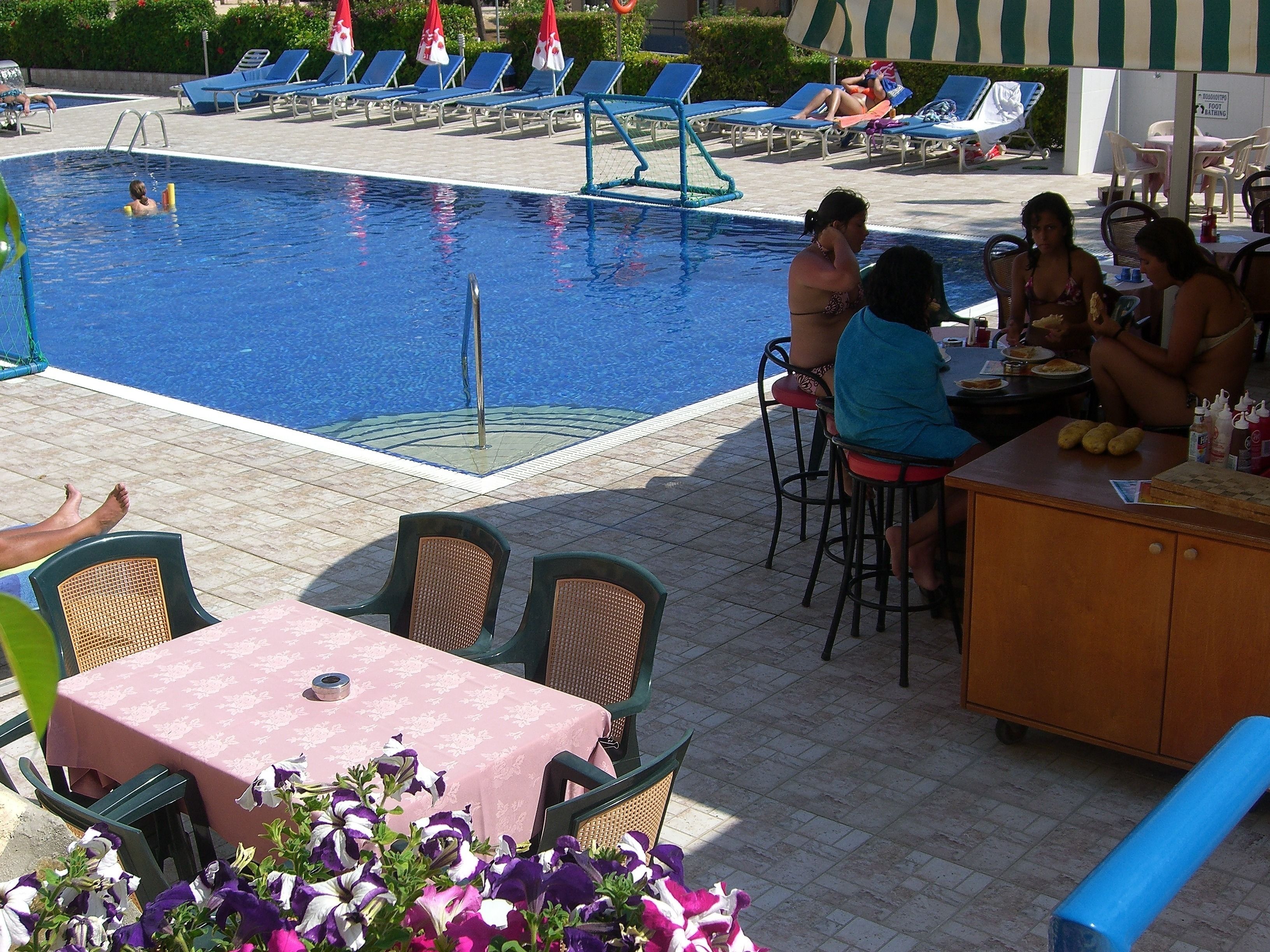 Ett område vid poolen med solstolar, en pool och en bar med barstolar och ett bord.
