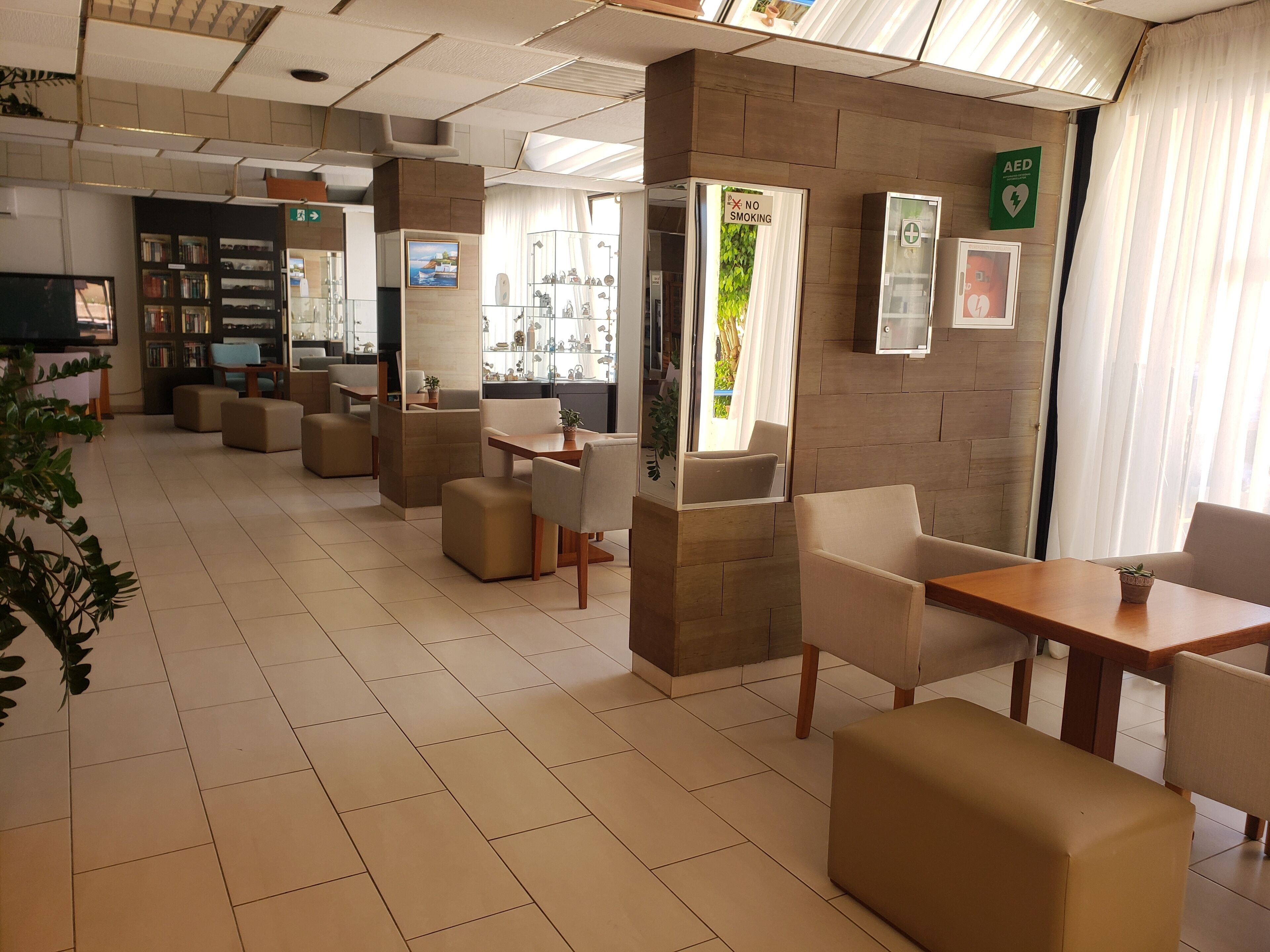 A modern hotel lobby with a clean, minimalist design, featuring comfortable seating areas, a reception desk, and visible amenities like an AED sign.