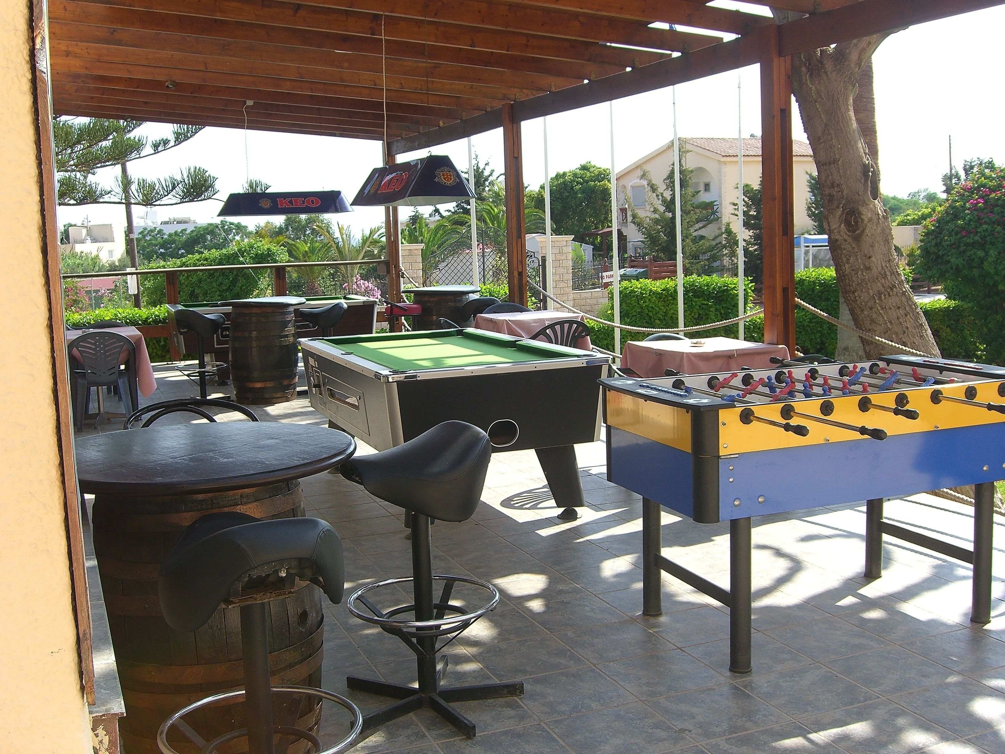 Zona de bar al aire libre con mesa de billar, mesa de futbolín y asientos.