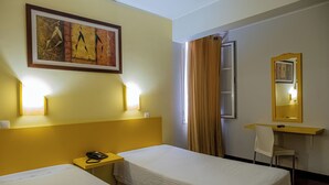 A hotel room with two beds, a desk, a chair, a telephone, and a painting on the wall.
