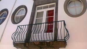 A building with a window featuring a white frame and a red curtain, a black wrought-iron balcony, and circular windows on the facade.