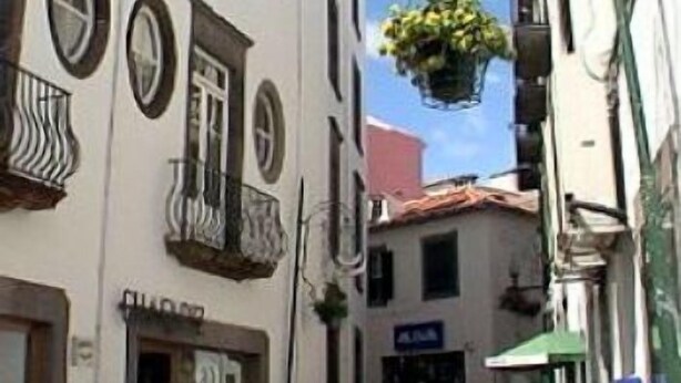 A narrow street with buildings on either side, featuring balconies and a hanging plant.