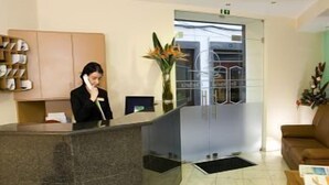 A reception area with a marble counter, a receptionist, a plant, and a brown leather couch.