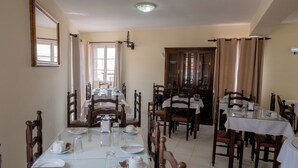 A dining area with multiple tables set for service, wooden chairs, and a large mirror on the wall.