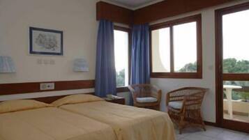Habitación de hotel con dos camas, una silla, una mesa y un ventanal grande con cortinas.